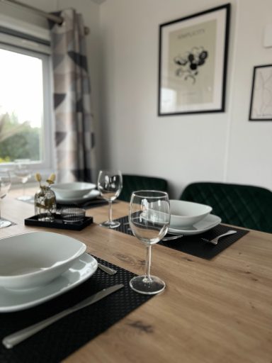 Elegant gedeckter Esstisch mit weißen Tellern und Gläsern, umgeben von Fenstern.